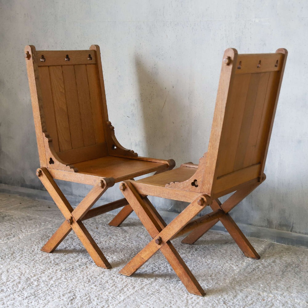 A pair of warm brown oak Glastonbury chairs featuring panelled backs with trefoil cut-outs and exposed pegged X-frame legs. View IX