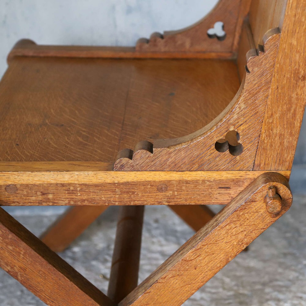 A pair of warm brown oak Glastonbury chairs featuring panelled backs with trefoil cut-outs and exposed pegged X-frame legs. View XI
