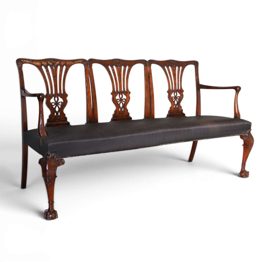 An Edwardian mahogany three-seater settee featuring three carved Chippendale-style pierced back splats, curved armrests, cabriole front legs with ball and claw feet, and a dark upholstered seat.