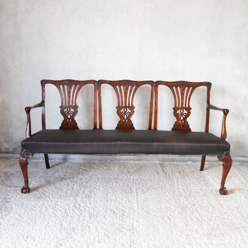 An Edwardian mahogany three-seater settee featuring three carved Chippendale-style pierced back splats, curved armrests, cabriole front legs with ball and claw feet, and a dark upholstered seat. View II