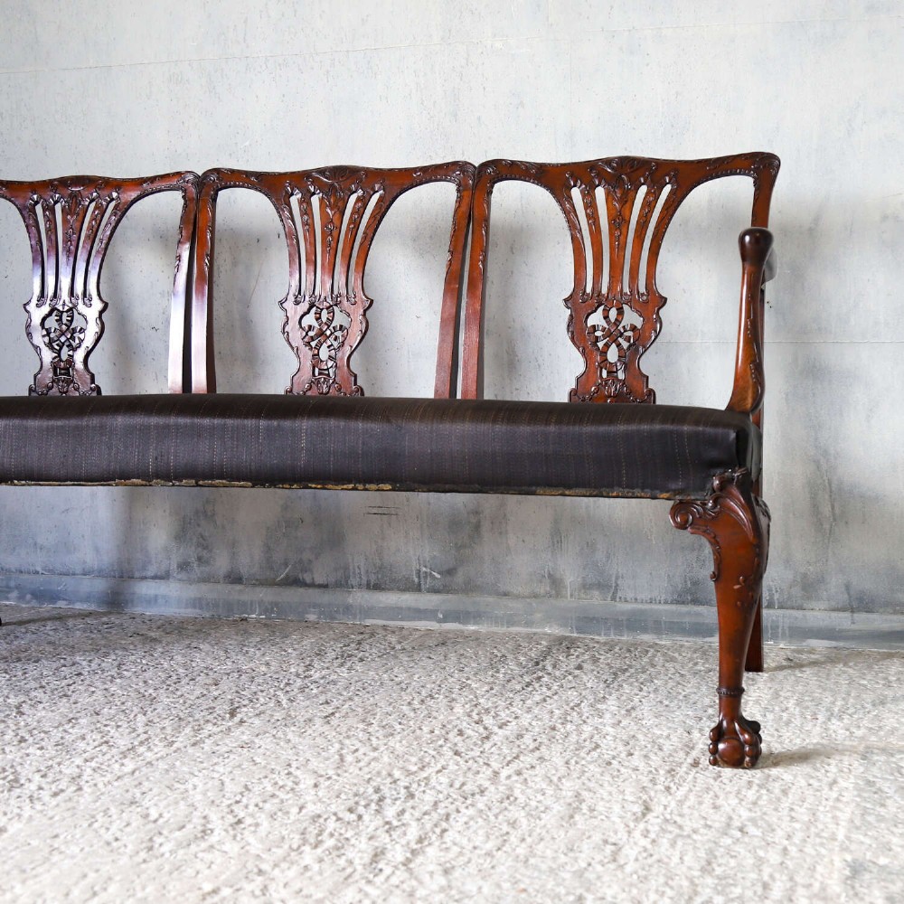 An Edwardian mahogany three-seater settee featuring three carved Chippendale-style pierced back splats, curved armrests, cabriole front legs with ball and claw feet, and a dark upholstered seat. View VIII