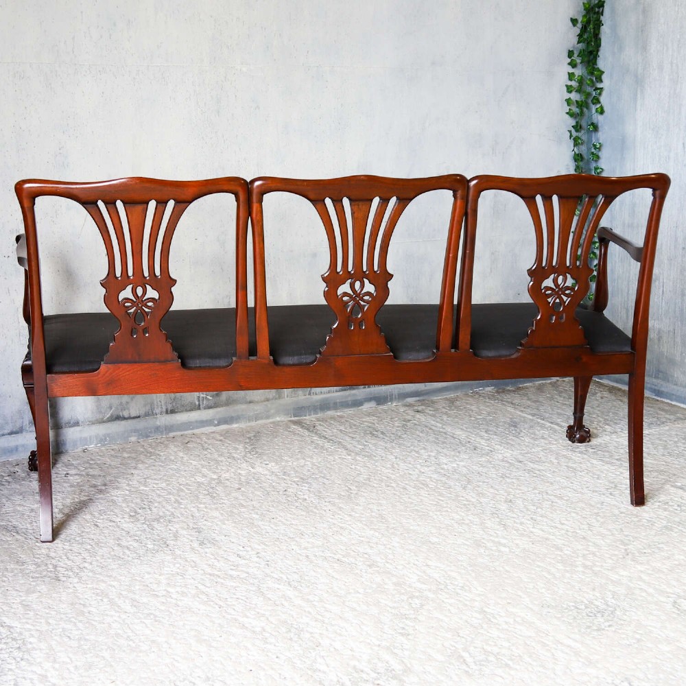 An Edwardian mahogany three-seater settee featuring three carved Chippendale-style pierced back splats, curved armrests, cabriole front legs with ball and claw feet, and a dark upholstered seat. View XIV
