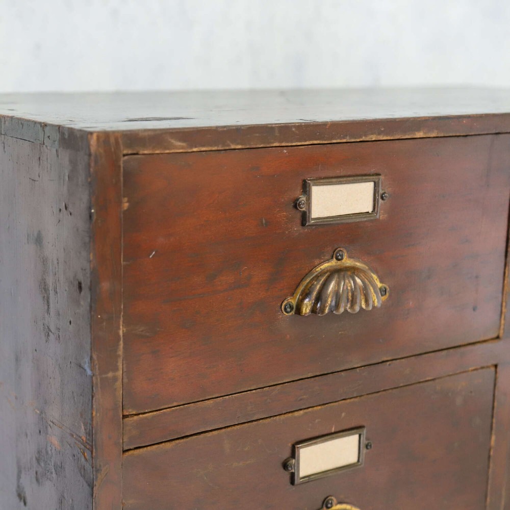 An antique Edwardian dark mahogany bank of twelve drawers featuring brass shell cup handles and label holders. View IV