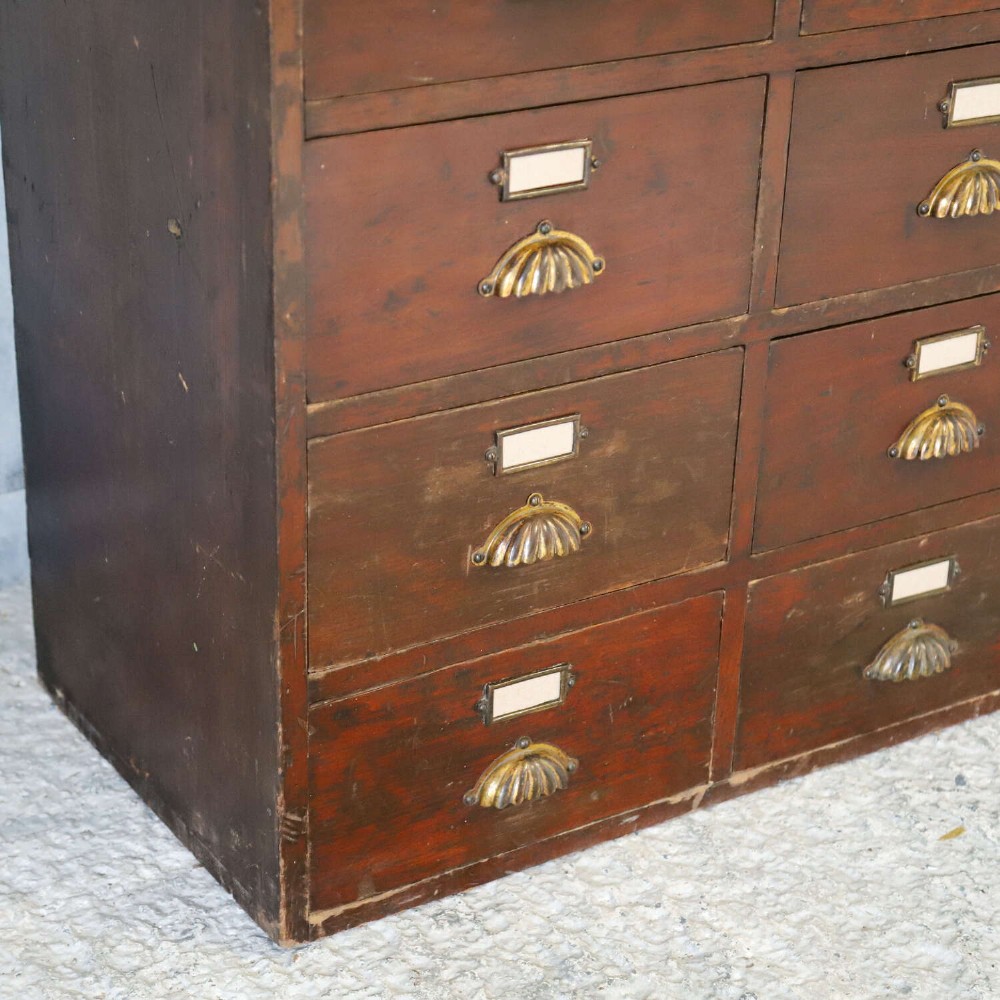 An antique Edwardian dark mahogany bank of twelve drawers featuring brass shell cup handles and label holders. View VIII