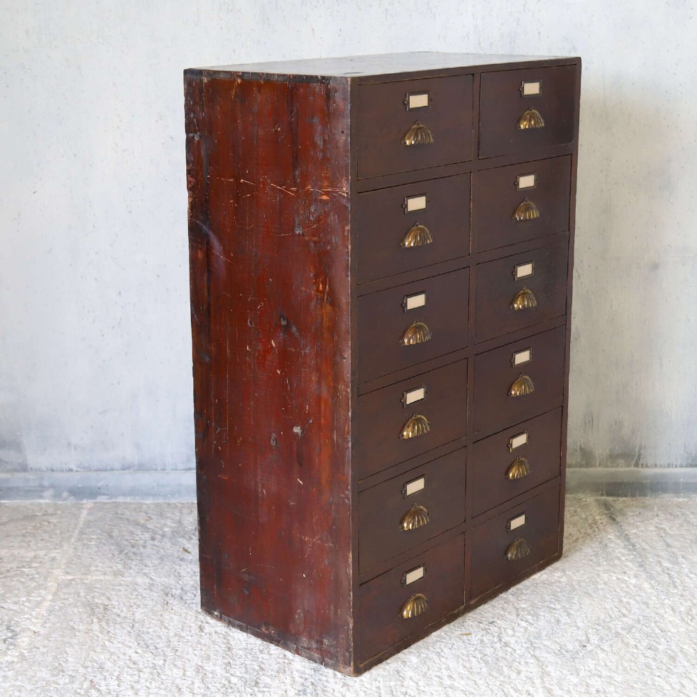 An antique Edwardian dark mahogany bank of twelve drawers featuring brass shell cup handles and label holders. View IX
