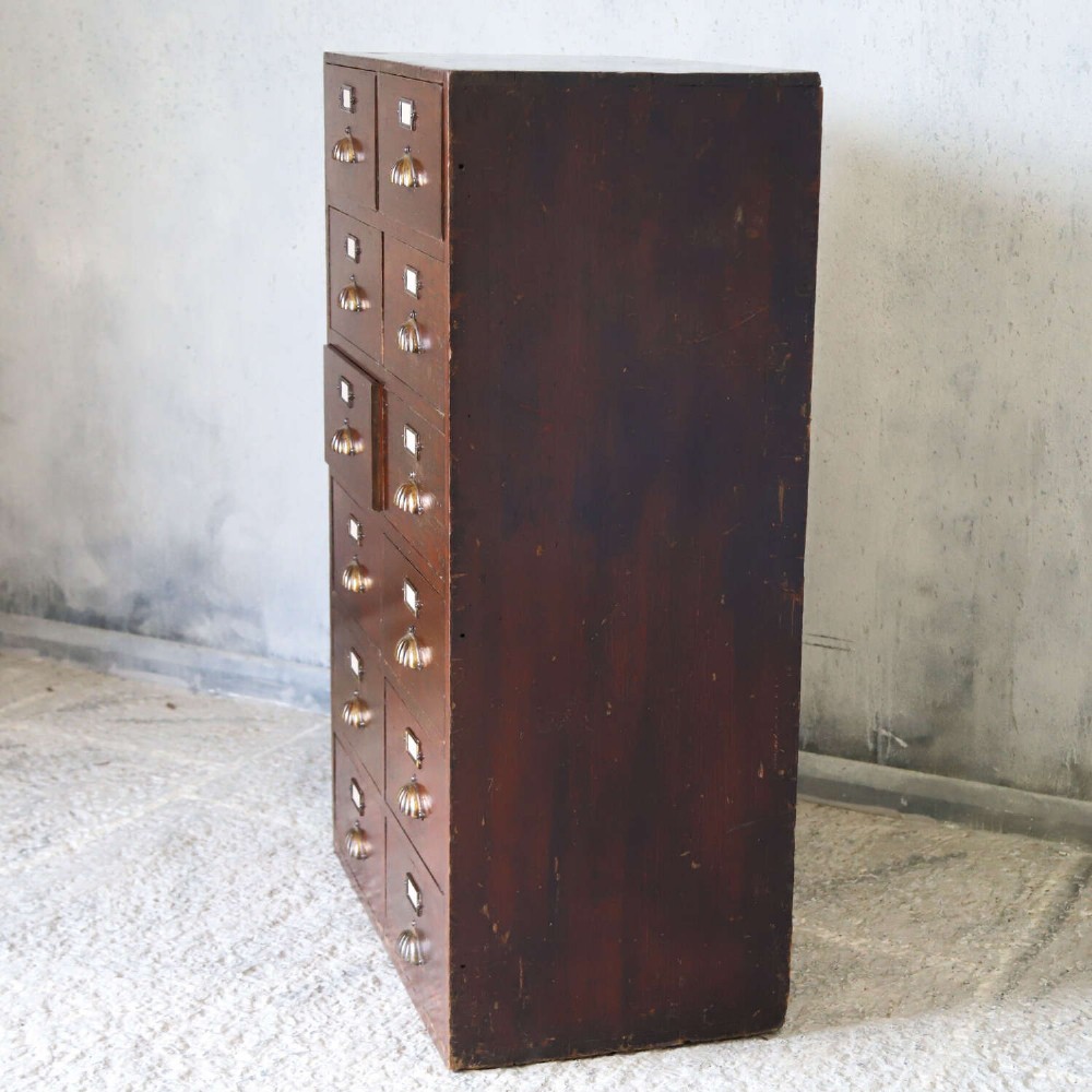 An antique Edwardian dark mahogany bank of twelve drawers featuring brass shell cup handles and label holders. View XI