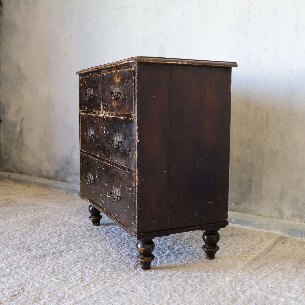 An antique pine chest of drawers featuring a dark brown scumble paint finish, Art Nouveau brass drop handles, two short drawers over two long drawers, and turned feet. View V