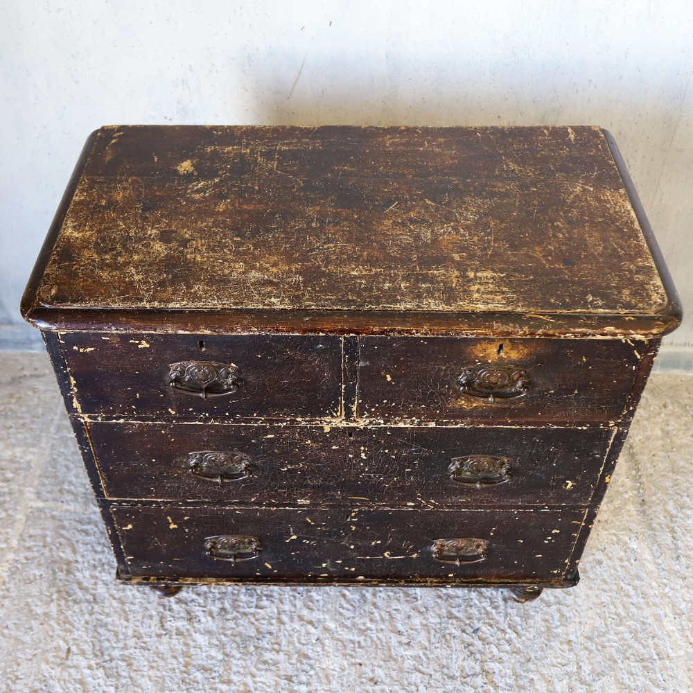 An antique pine chest of drawers featuring a dark brown scumble paint finish, Art Nouveau brass drop handles, two short drawers over two long drawers, and turned feet. View VII