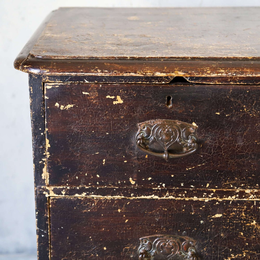 An antique pine chest of drawers featuring a dark brown scumble paint finish, Art Nouveau brass drop handles, two short drawers over two long drawers, and turned feet. View XI