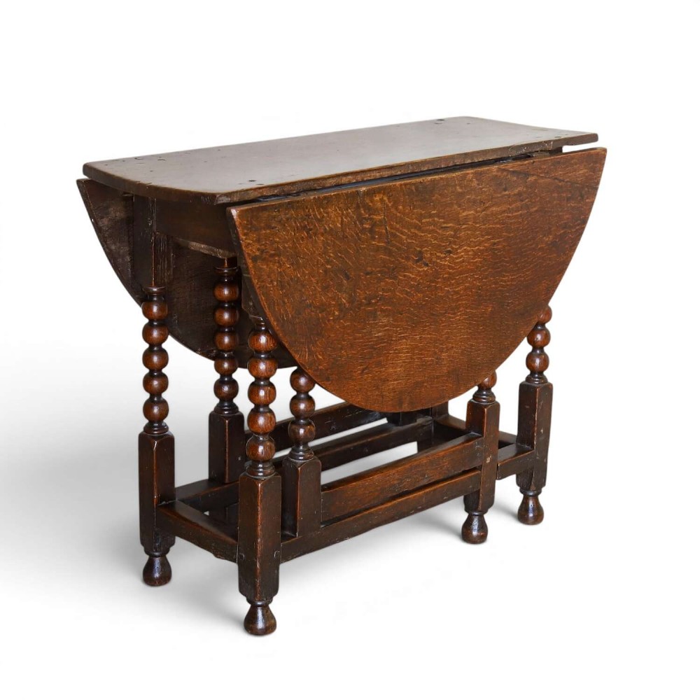 A dark oak gateleg table featuring two hinged drop leaves, bobbin turned legs, and lower box stretchers.