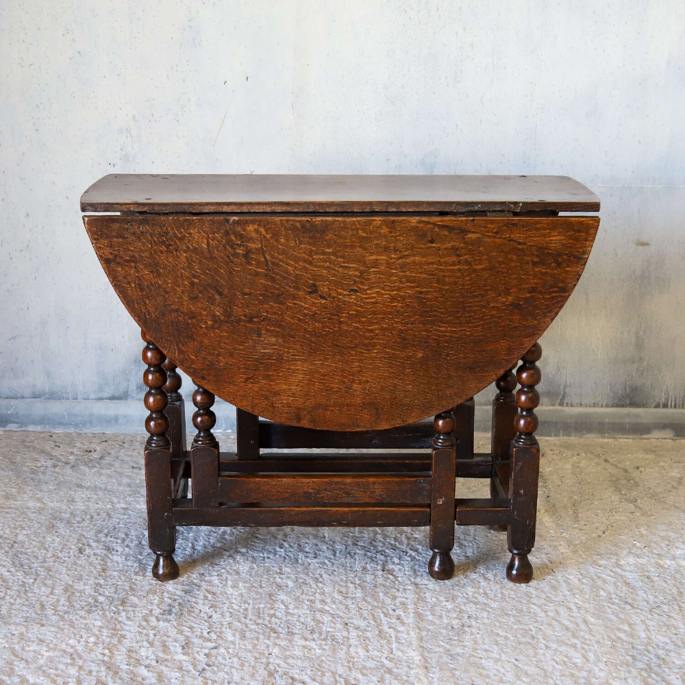 A dark oak gateleg table featuring two hinged drop leaves, bobbin turned legs, and lower box stretchers. View II