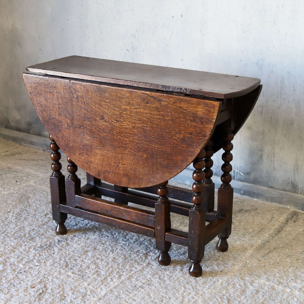 A dark oak gateleg table featuring two hinged drop leaves, bobbin turned legs, and lower box stretchers. View III
