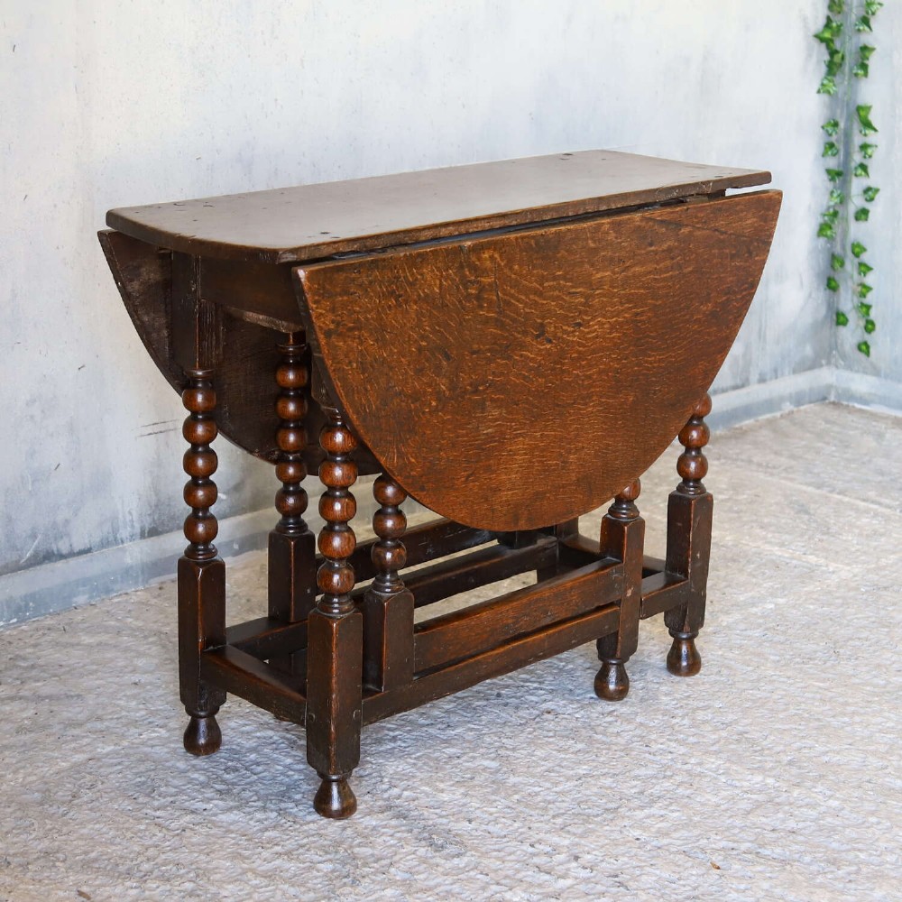 A dark oak gateleg table featuring two hinged drop leaves, bobbin turned legs, and lower box stretchers. View IV