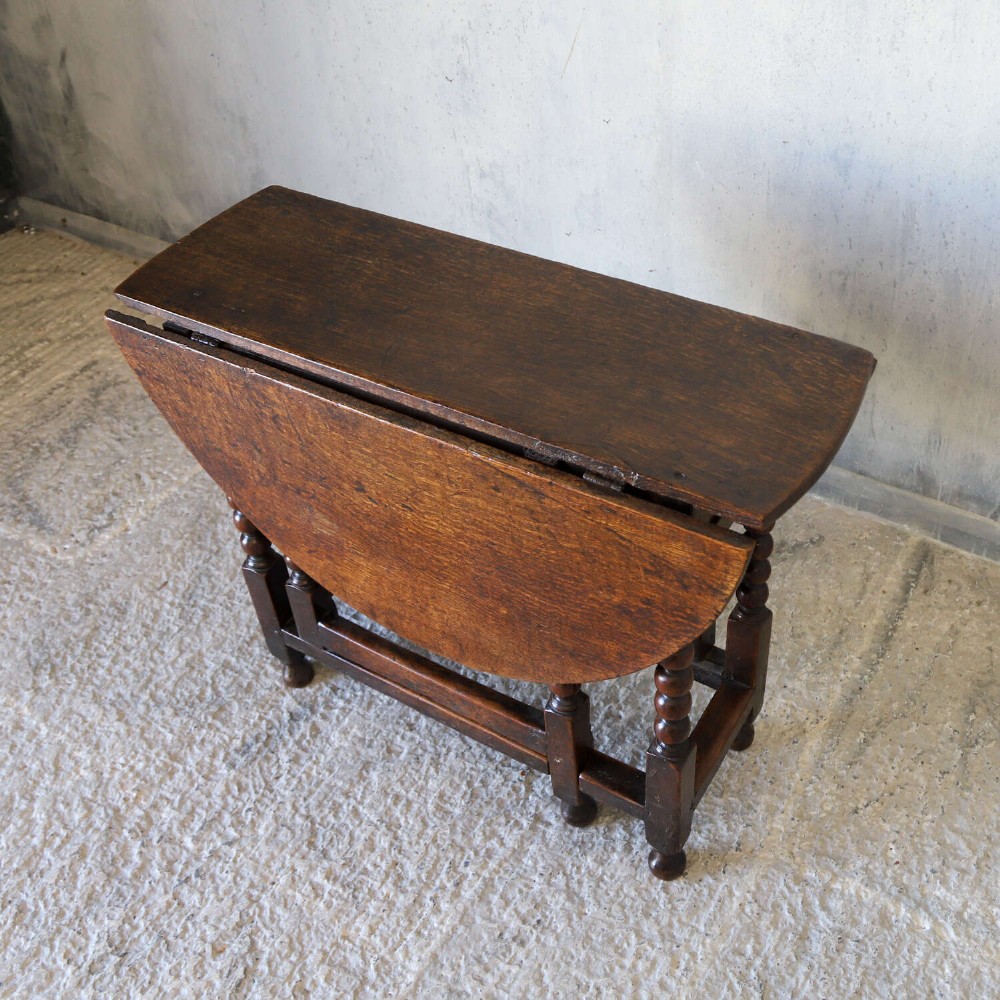 A dark oak gateleg table featuring two hinged drop leaves, bobbin turned legs, and lower box stretchers. View V