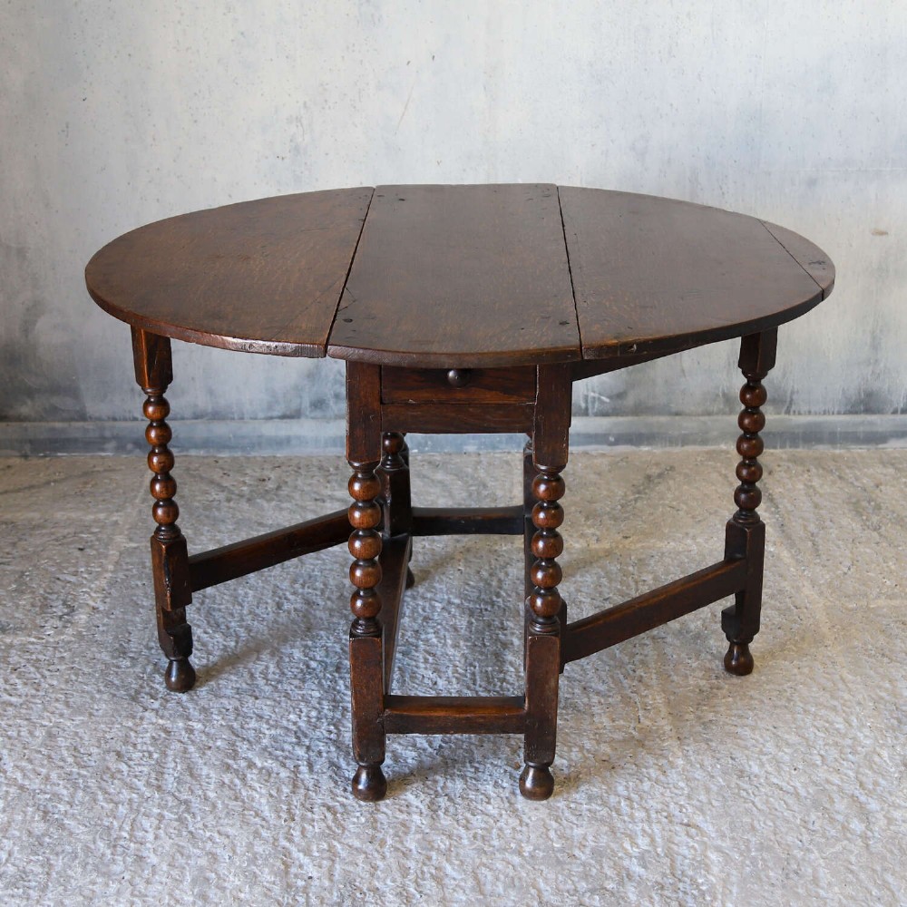A dark oak gateleg table featuring two hinged drop leaves, bobbin turned legs, and lower box stretchers. View XI