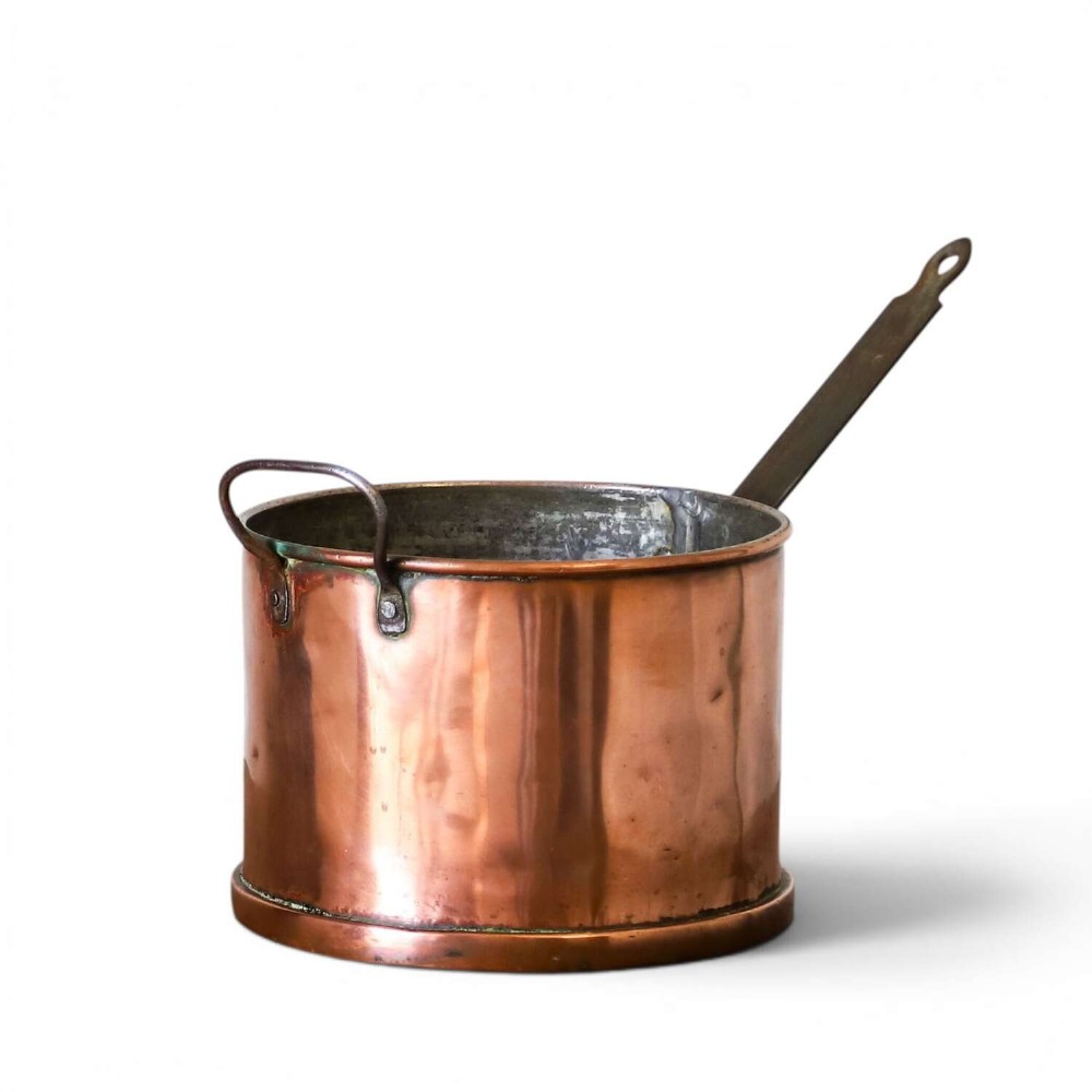 A mid-19th century hand-beaten heavy gauge copper saucepan featuring a long flat iron handle, a side loop handle, and a tinned interior.