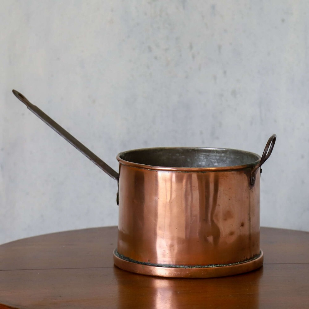 A mid-19th century hand-beaten heavy gauge copper saucepan featuring a long flat iron handle, a side loop handle, and a tinned interior. View II