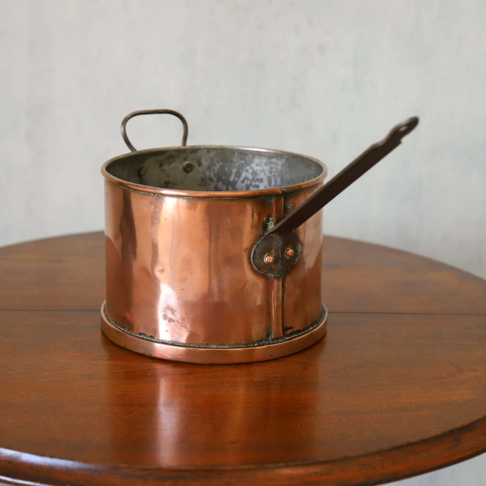 A mid-19th century hand-beaten heavy gauge copper saucepan featuring a long flat iron handle, a side loop handle, and a tinned interior. View VI
