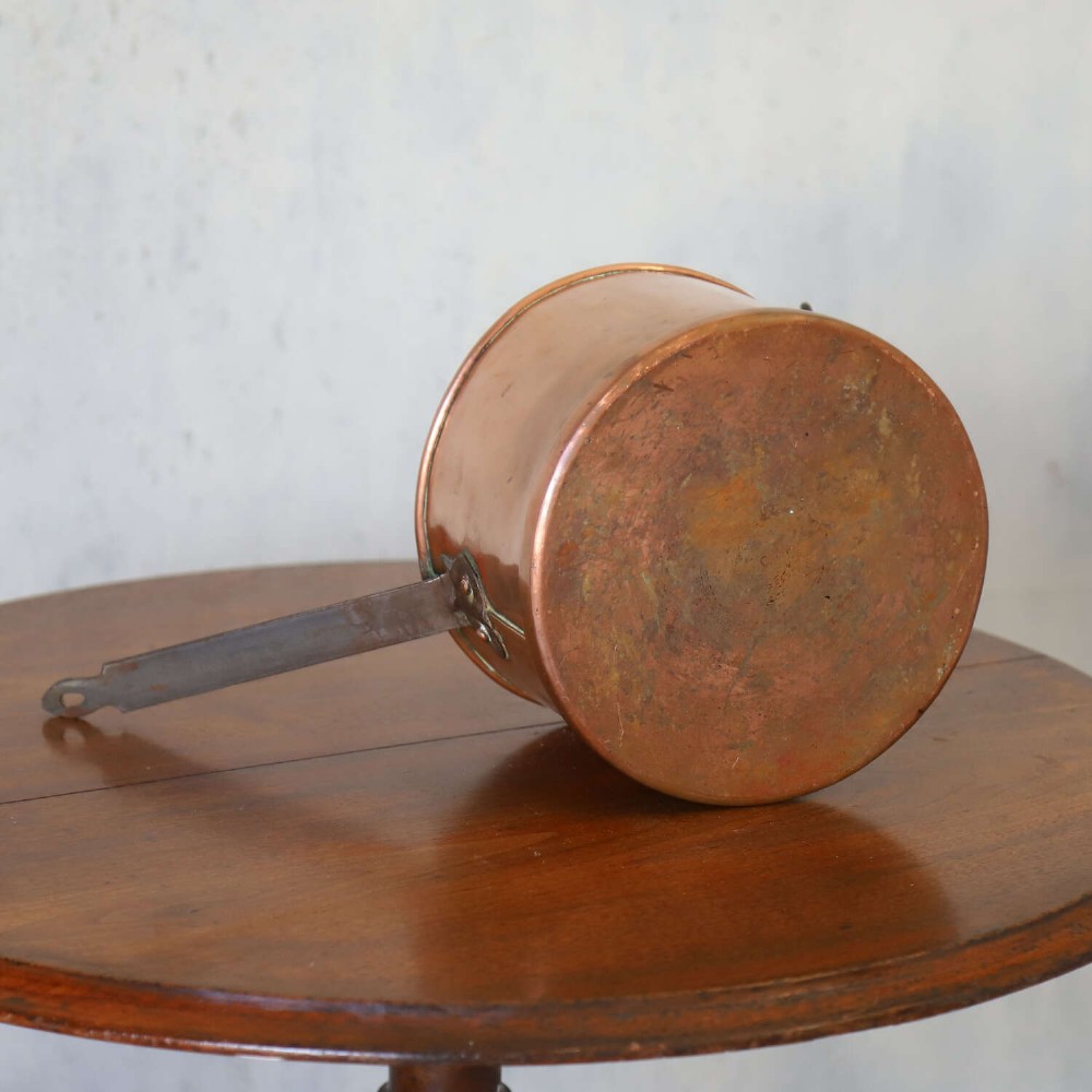A mid-19th century hand-beaten heavy gauge copper saucepan featuring a long flat iron handle, a side loop handle, and a tinned interior. View IX