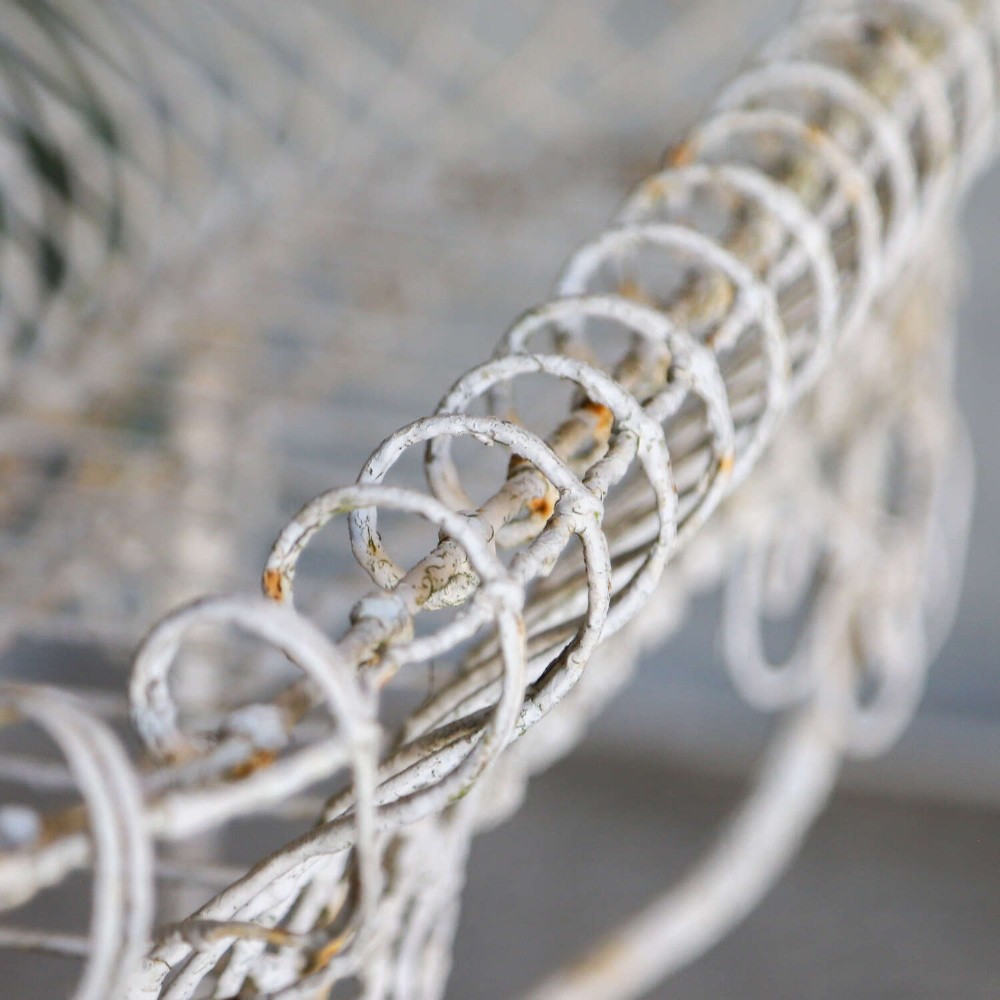 A 19th-century distressed white painted wrought iron plant stand featuring a wire lattice basket top over scrollwork legs. View VII