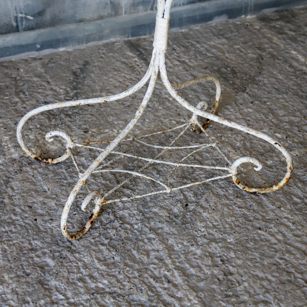 A 19th-century distressed white painted wrought iron plant stand featuring a wire lattice basket top over scrollwork legs. View VIII