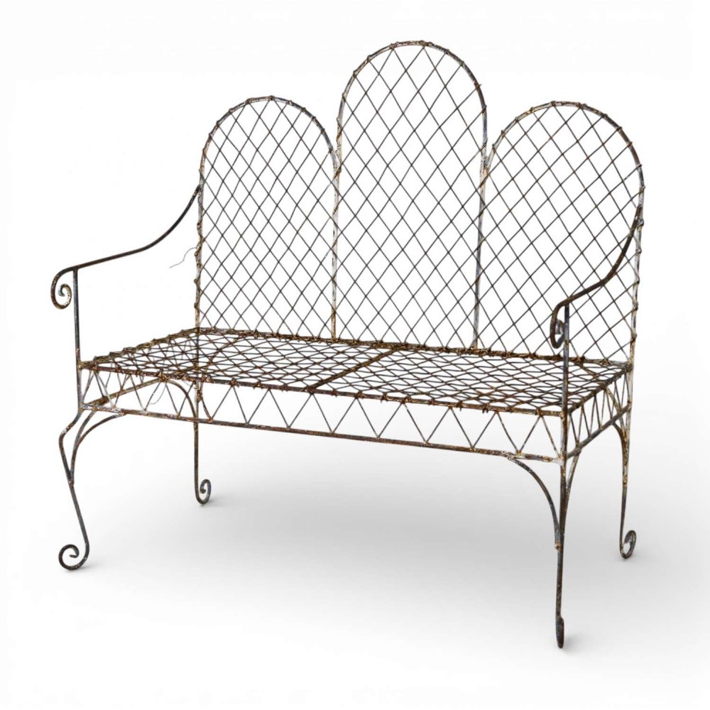 A French Gothic-influenced metal garden bench featuring a triple arched wirework backrest, lattice seat, and scrolled armrests and legs with a weathered, distressed paint finish.