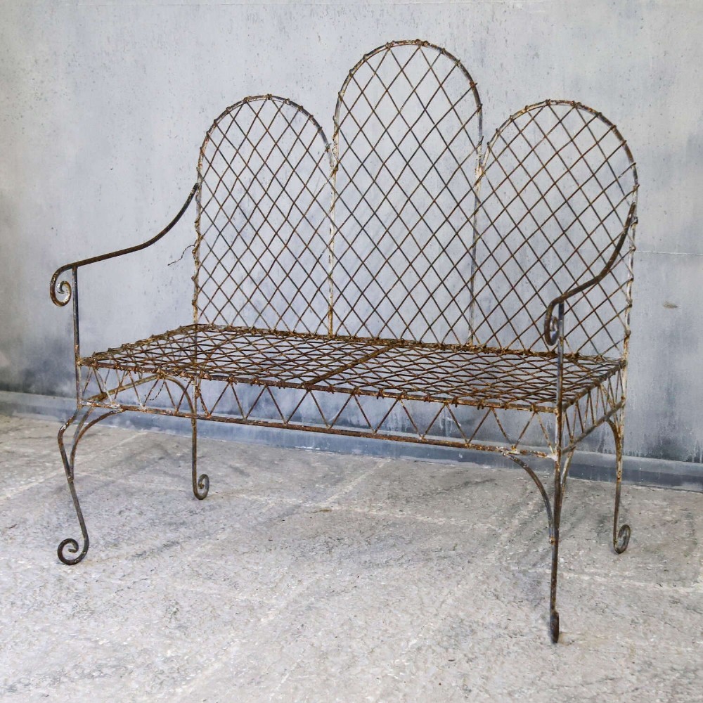 A French Gothic-influenced metal garden bench featuring a triple arched wirework backrest, lattice seat, and scrolled armrests and legs with a weathered, distressed paint finish. View IV