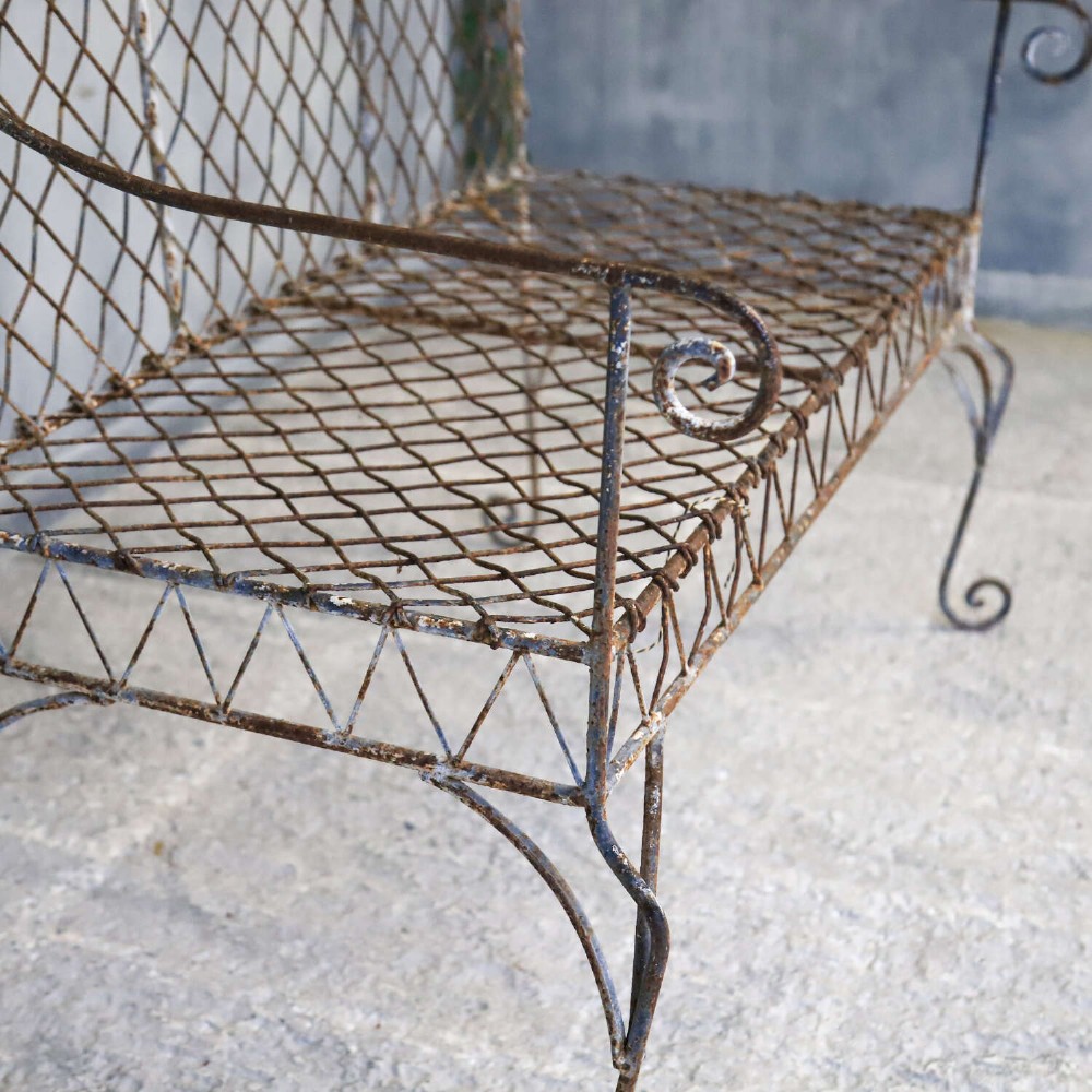 A French Gothic-influenced metal garden bench featuring a triple arched wirework backrest, lattice seat, and scrolled armrests and legs with a weathered, distressed paint finish. View X