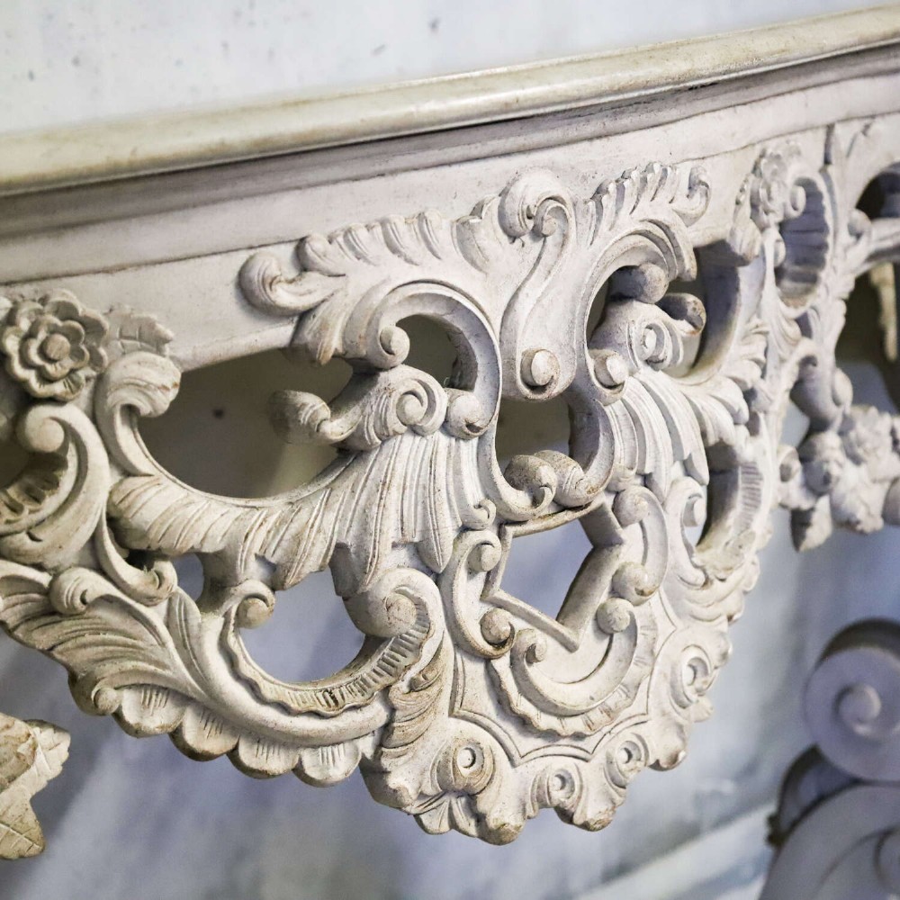A pair of 1930s French wall console tables with intricate carved Rococo scrollwork in an antique white painted finish. View IX