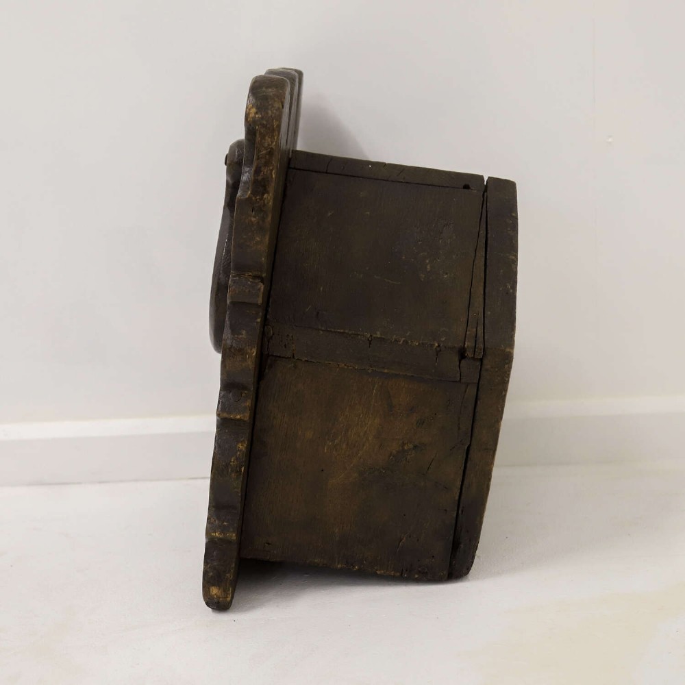 A dark brown 17th or 18th-century carved oak salt box featuring a shaped backboard with a circular hanging aperture and a sloping hinged lid. View IX