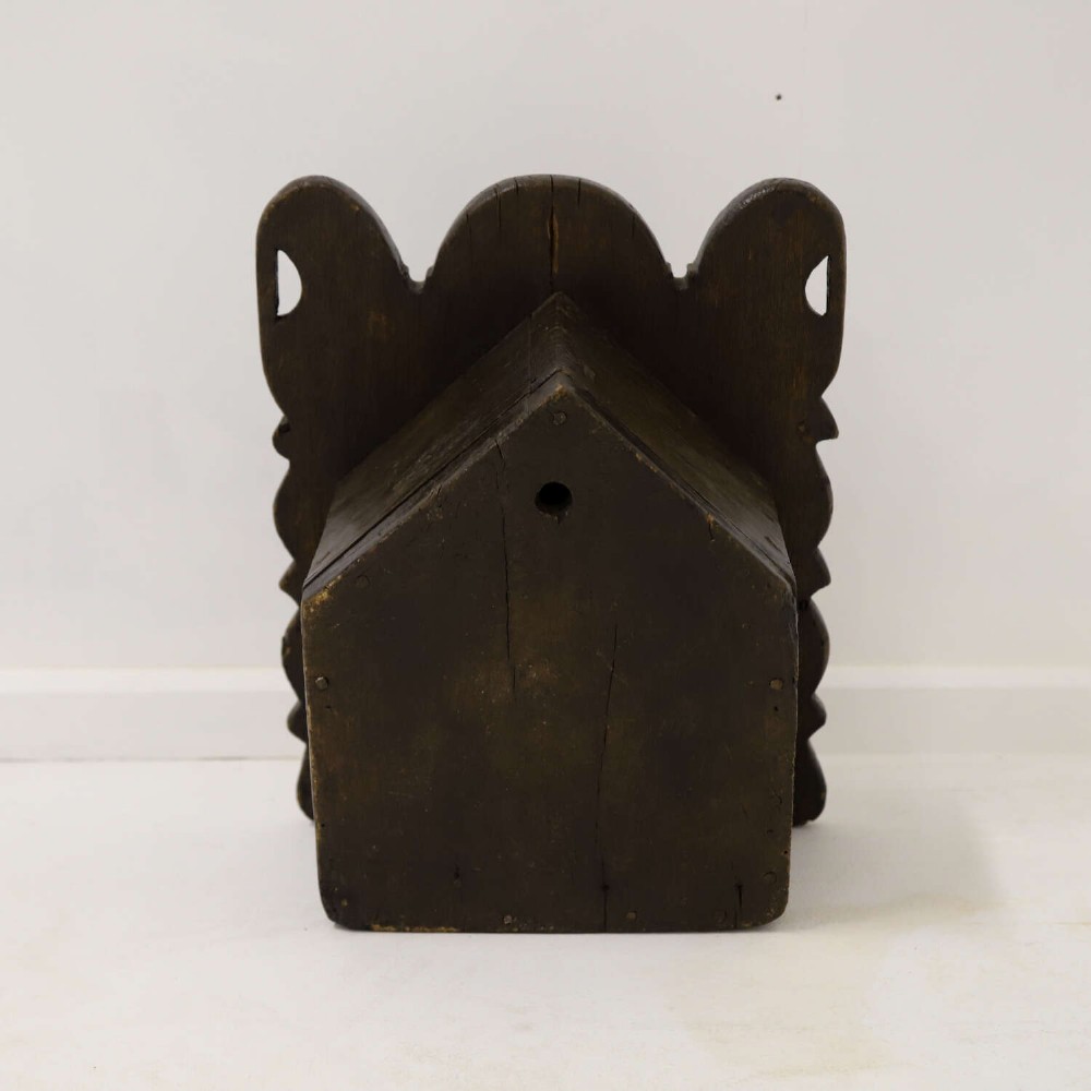 A dark brown 17th or 18th-century carved oak salt box featuring a shaped backboard with a circular hanging aperture and a sloping hinged lid. View X