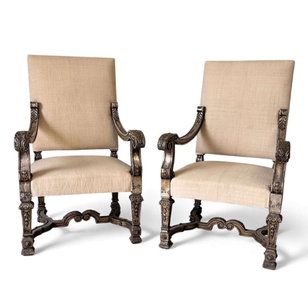 A pair of 19th-century Baroque-style throne armchairs featuring carved giltwood frames and neutral linen upholstery.