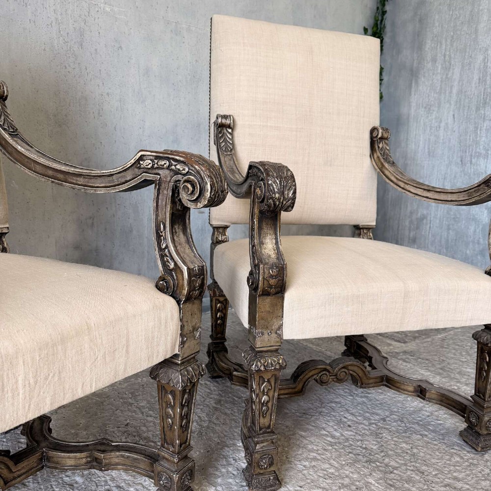 A pair of 19th-century Baroque-style throne armchairs featuring carved giltwood frames and neutral linen upholstery. View X