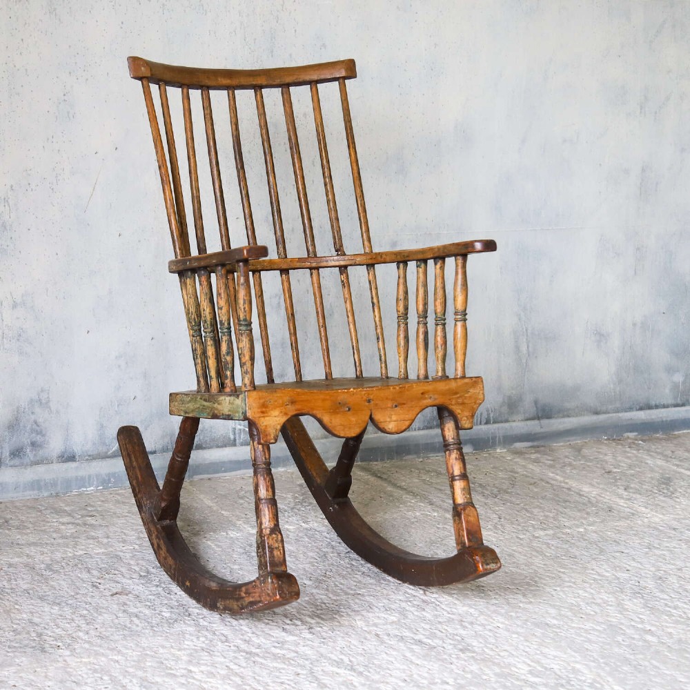 A 19th-century primitive comb-back rocking chair crafted from wood with tall back spindles, turned arm supports, and curved wooden runners. View II