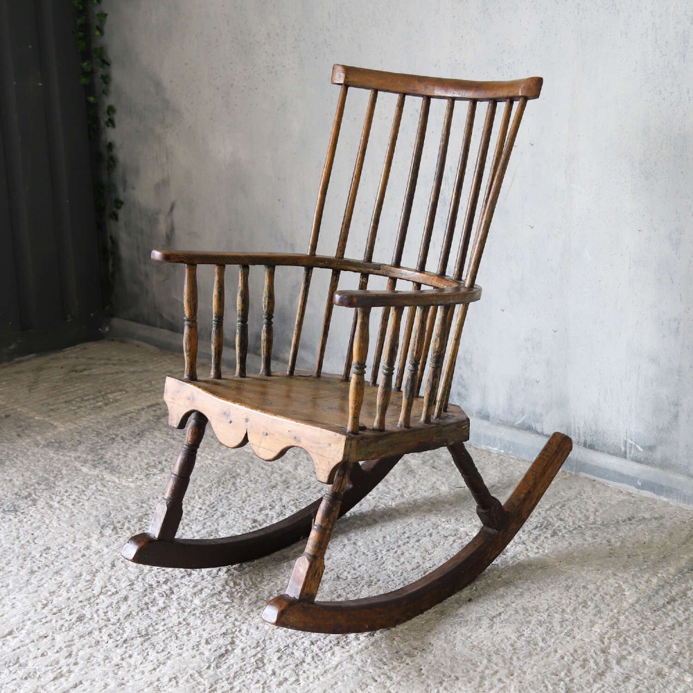 A 19th-century primitive comb-back rocking chair crafted from wood with tall back spindles, turned arm supports, and curved wooden runners. View III