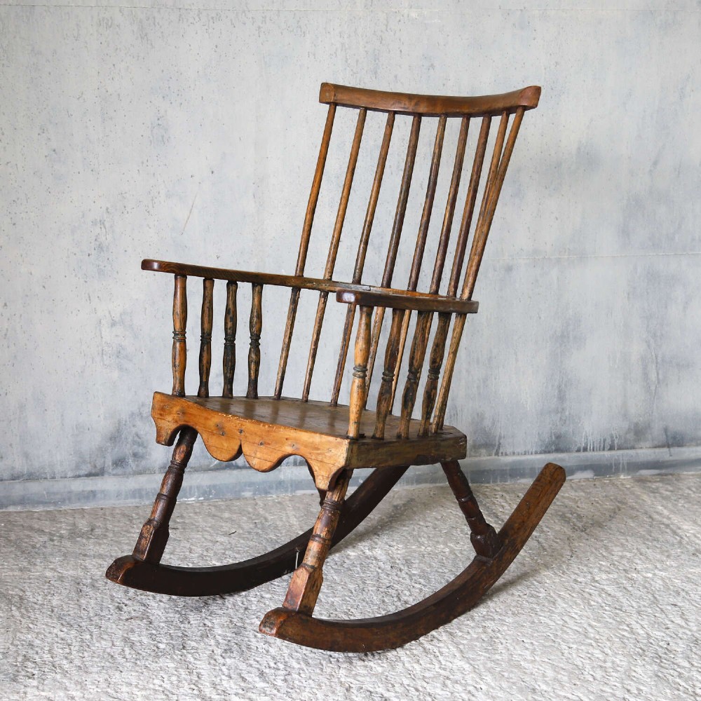 A 19th-century primitive comb-back rocking chair crafted from wood with tall back spindles, turned arm supports, and curved wooden runners. View IV