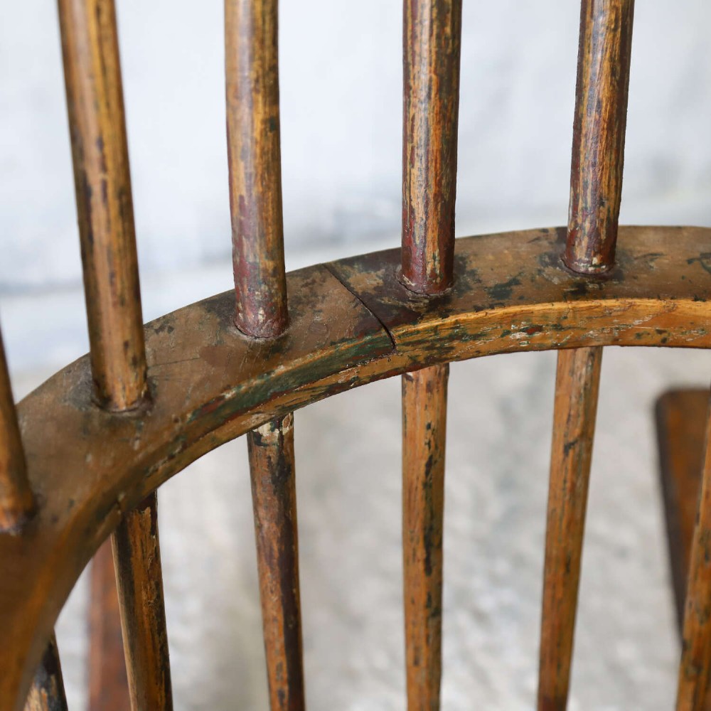 A 19th-century primitive comb-back rocking chair crafted from wood with tall back spindles, turned arm supports, and curved wooden runners. View V