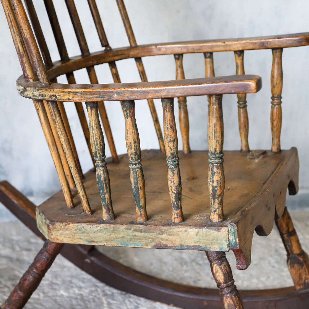 A 19th-century primitive comb-back rocking chair crafted from wood with tall back spindles, turned arm supports, and curved wooden runners. View VII