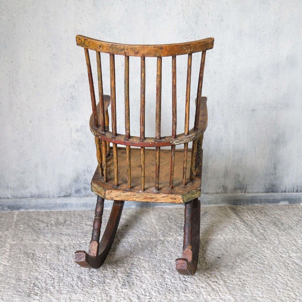 A 19th-century primitive comb-back rocking chair crafted from wood with tall back spindles, turned arm supports, and curved wooden runners. View X