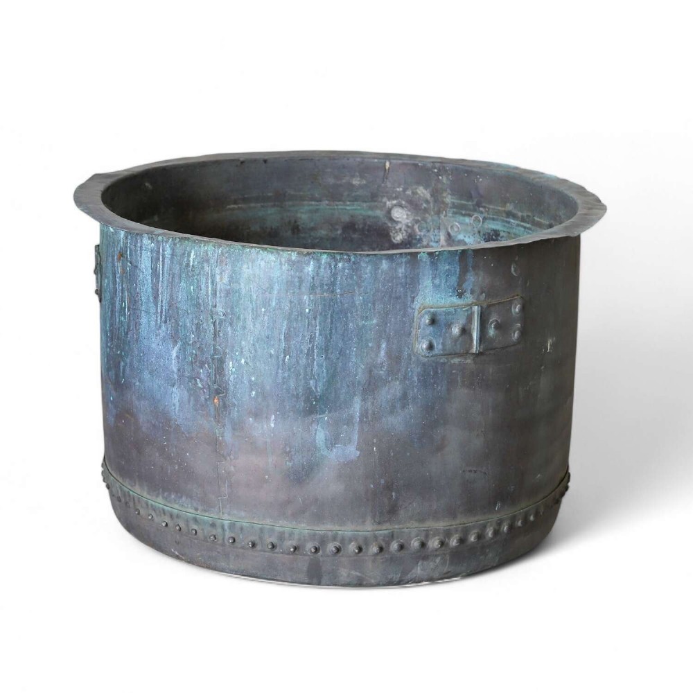 A large circular 19th-century copper tub featuring hand-riveted construction, side handles, and a blue-green verdigris patina.