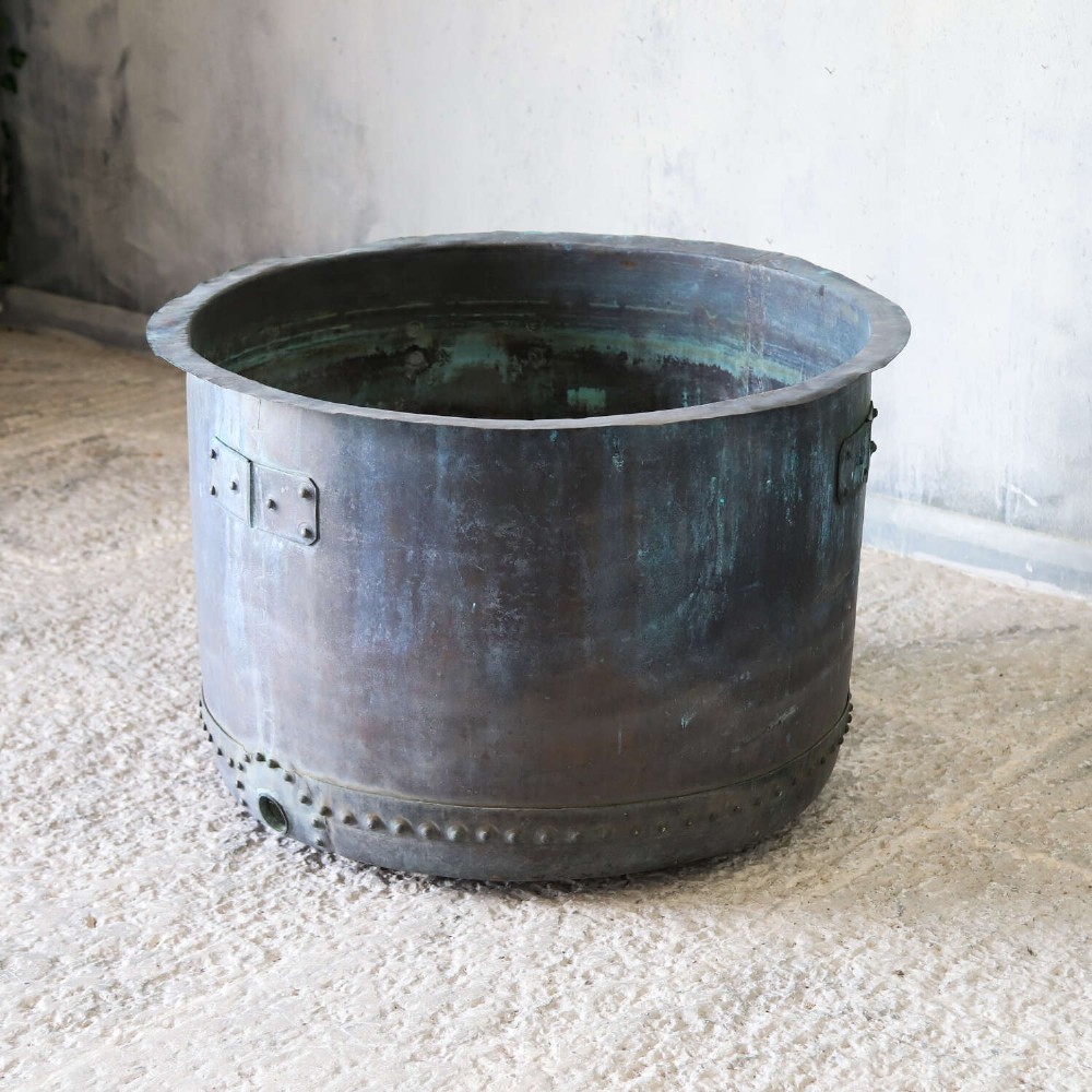 A large circular 19th-century copper tub featuring hand-riveted construction, side handles, and a blue-green verdigris patina. View X