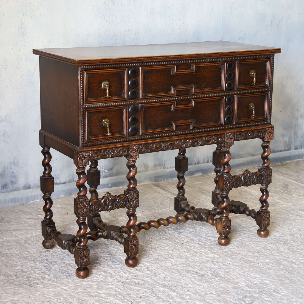 A dark oak Carolean Revival sideboard featuring two geometrically panelled drawers, intricate carving, and barley-twist legs connected by stretchers. View II