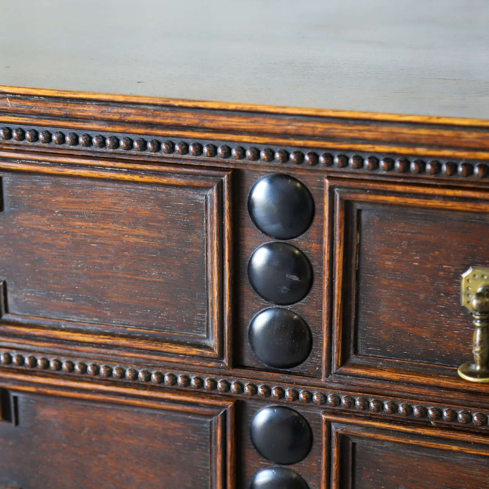 A dark oak Carolean Revival sideboard featuring two geometrically panelled drawers, intricate carving, and barley-twist legs connected by stretchers. View IV