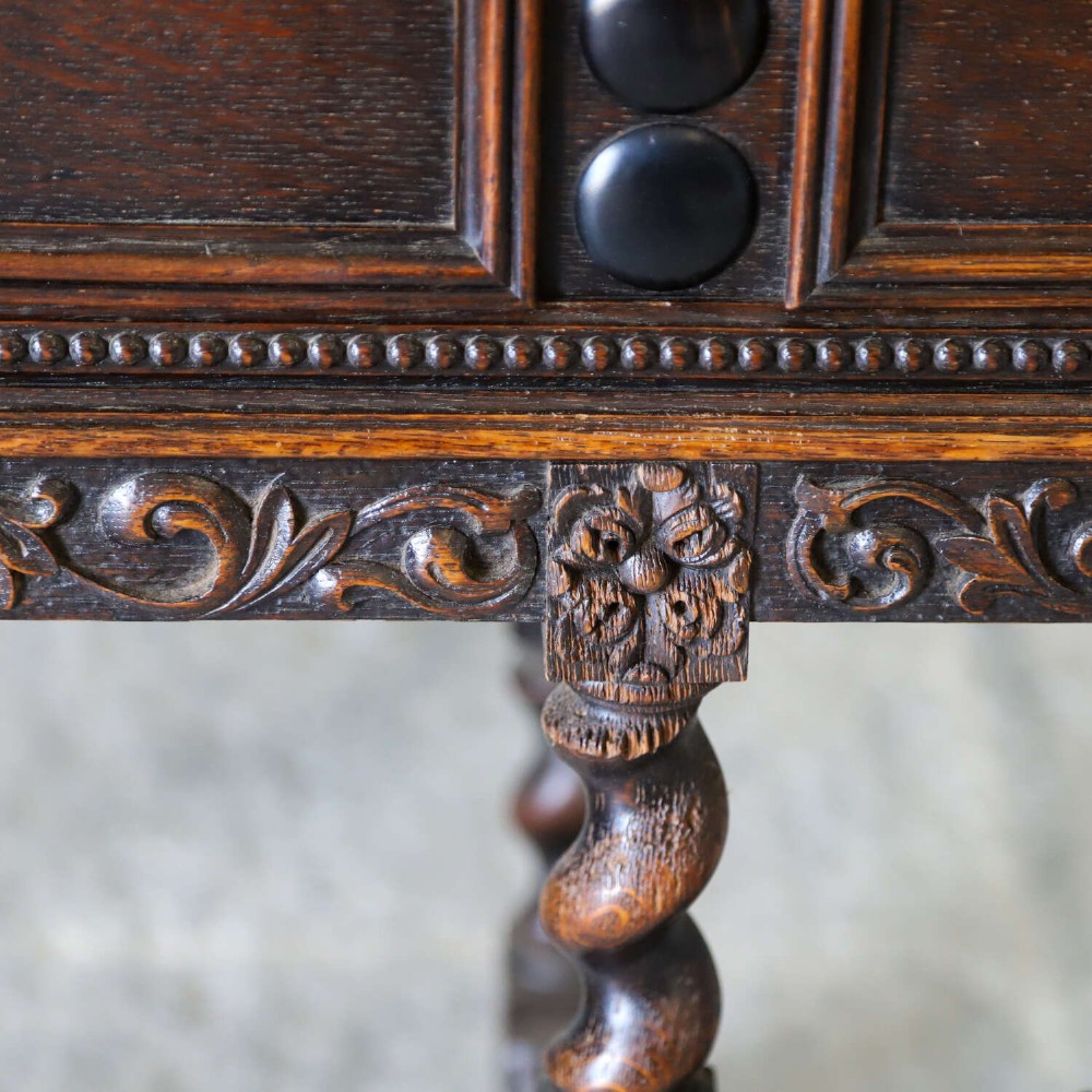 A dark oak Carolean Revival sideboard featuring two geometrically panelled drawers, intricate carving, and barley-twist legs connected by stretchers. View V