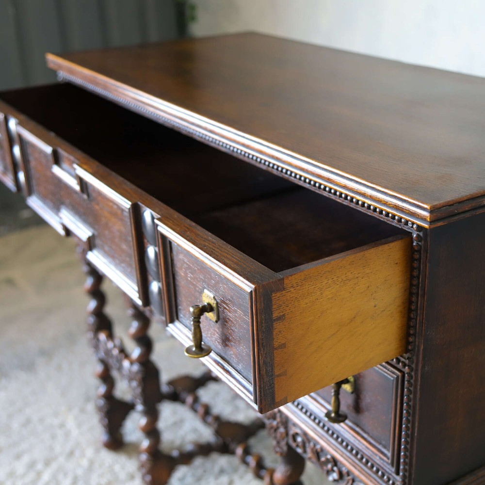 A dark oak Carolean Revival sideboard featuring two geometrically panelled drawers, intricate carving, and barley-twist legs connected by stretchers. View VII
