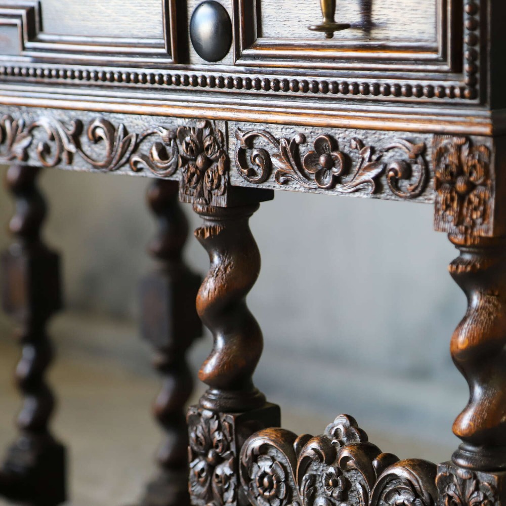 A dark oak Carolean Revival sideboard featuring two geometrically panelled drawers, intricate carving, and barley-twist legs connected by stretchers. View IX