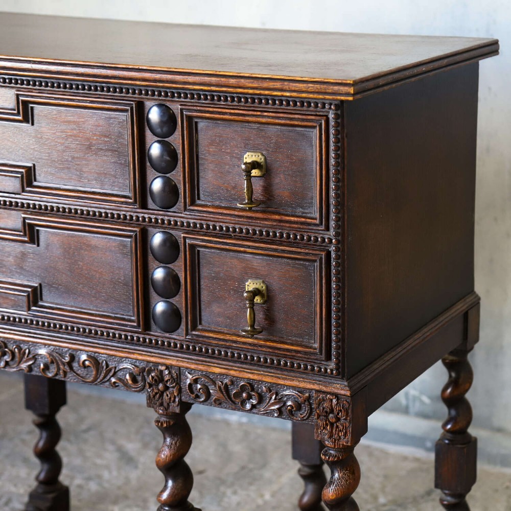 A dark oak Carolean Revival sideboard featuring two geometrically panelled drawers, intricate carving, and barley-twist legs connected by stretchers. View X