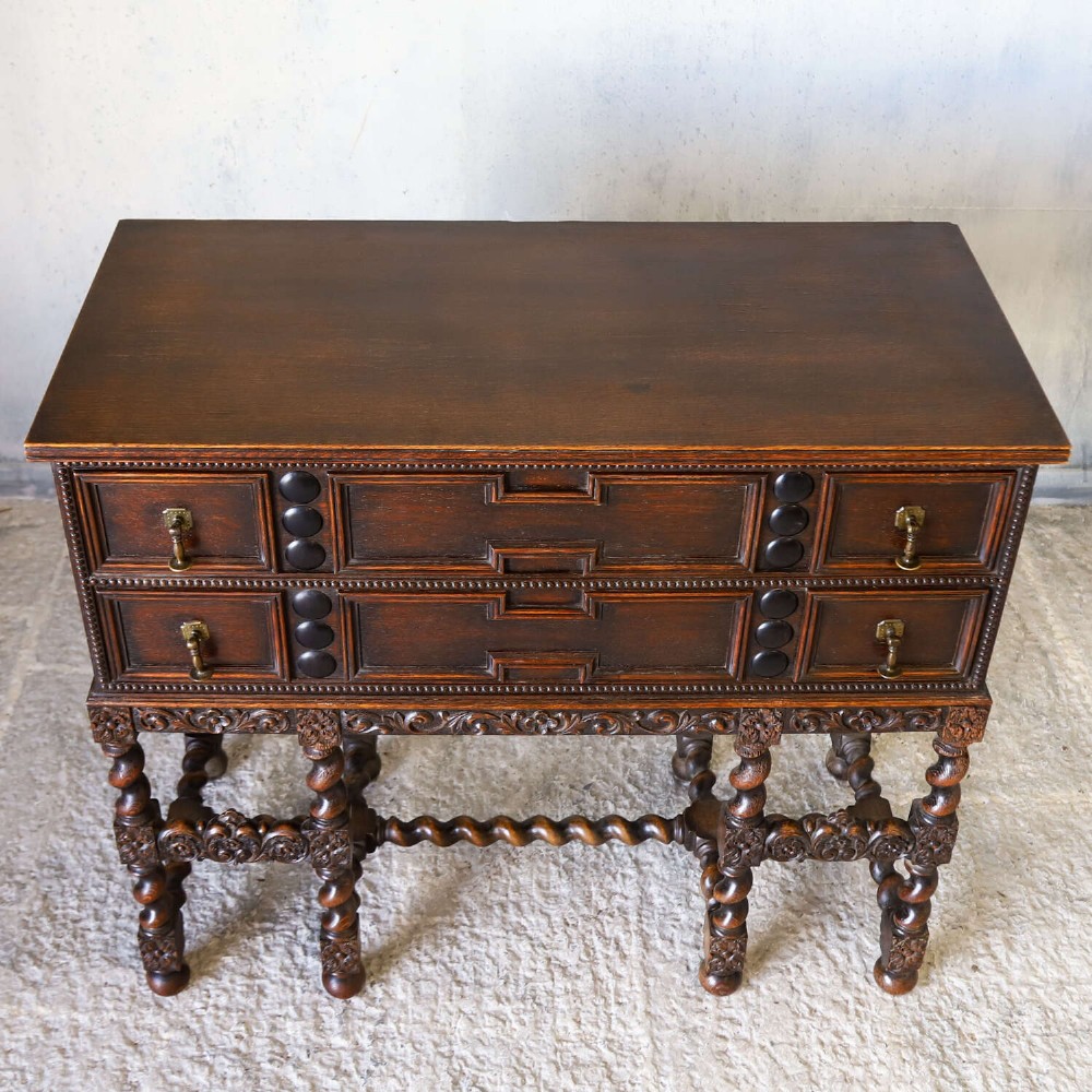 A dark oak Carolean Revival sideboard featuring two geometrically panelled drawers, intricate carving, and barley-twist legs connected by stretchers. View XII