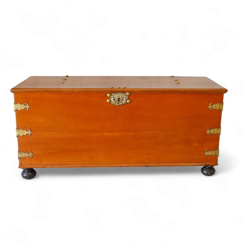 An 18th-century walnut colonial chest featuring decorative brass corner brackets, a central brass escutcheon, and dark turned feet.