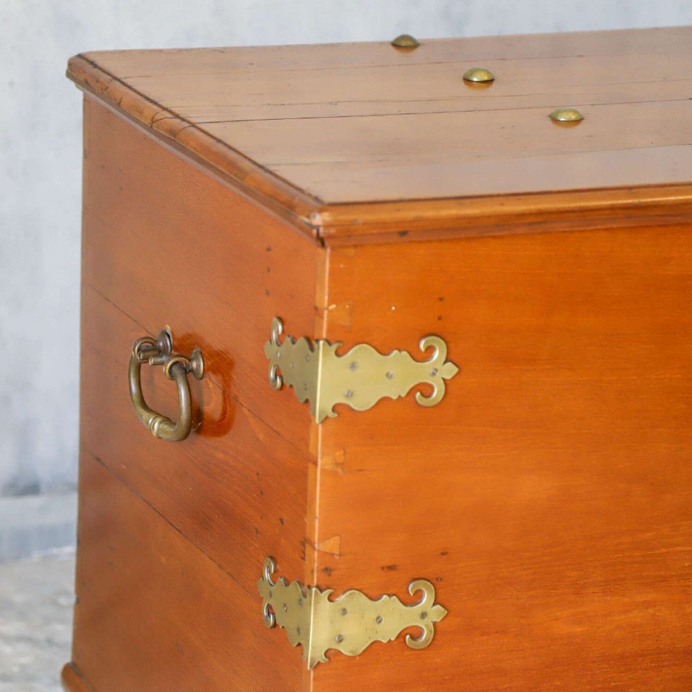 An 18th-century walnut colonial chest featuring decorative brass corner brackets, a central brass escutcheon, and dark turned feet. View IV